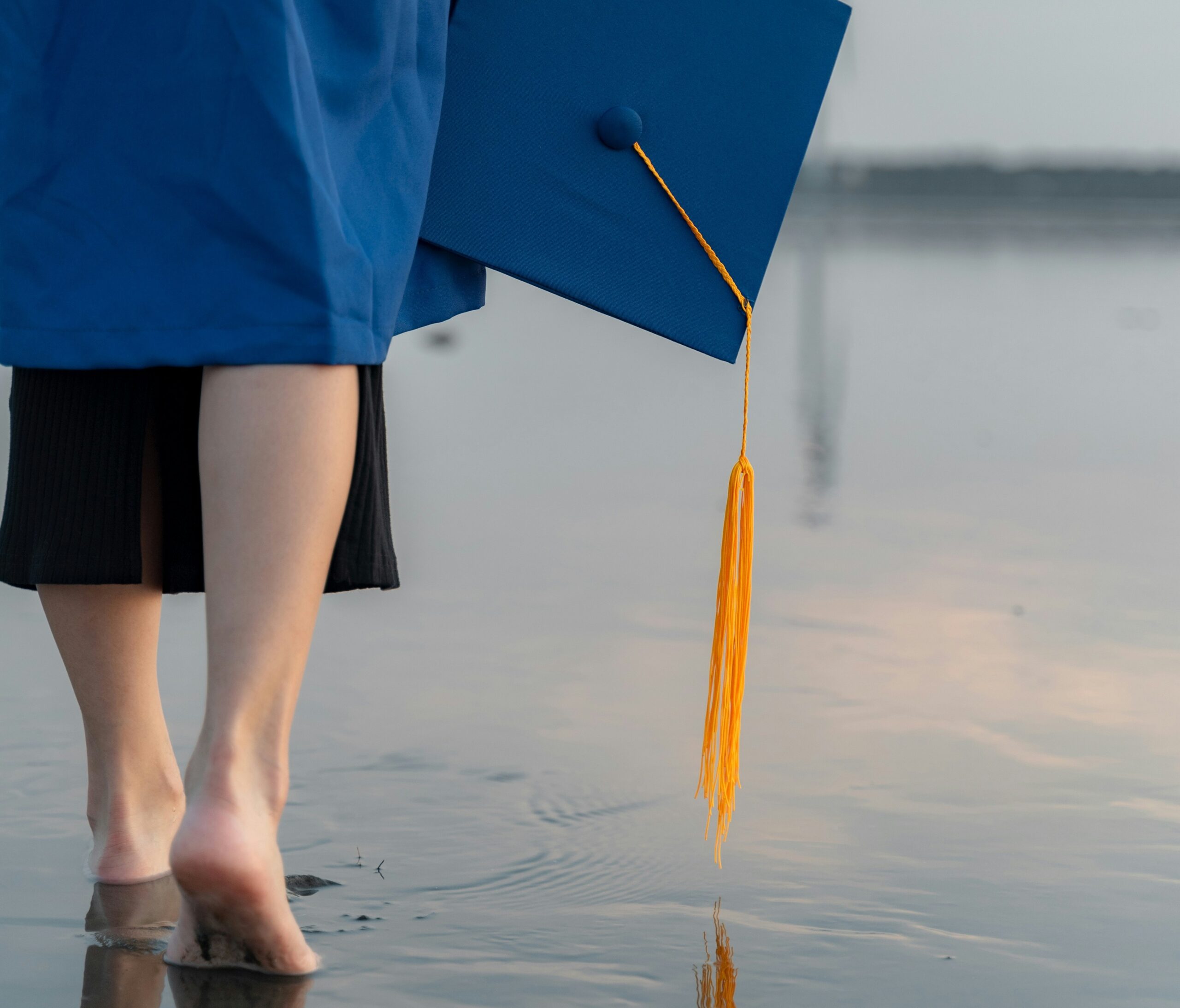 Photo of person walking on a beach in cap and gown